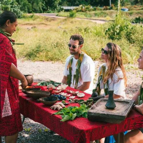 Une guide polynésienne en robe rouge montre des pigments naturels sur une table à trois participants.