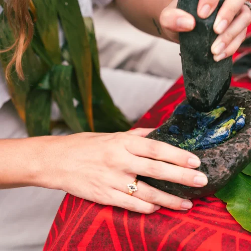 Mains d'une femme avec une bague, utilisant un pilon pour écraser des pigments bleus pour le Tapa.